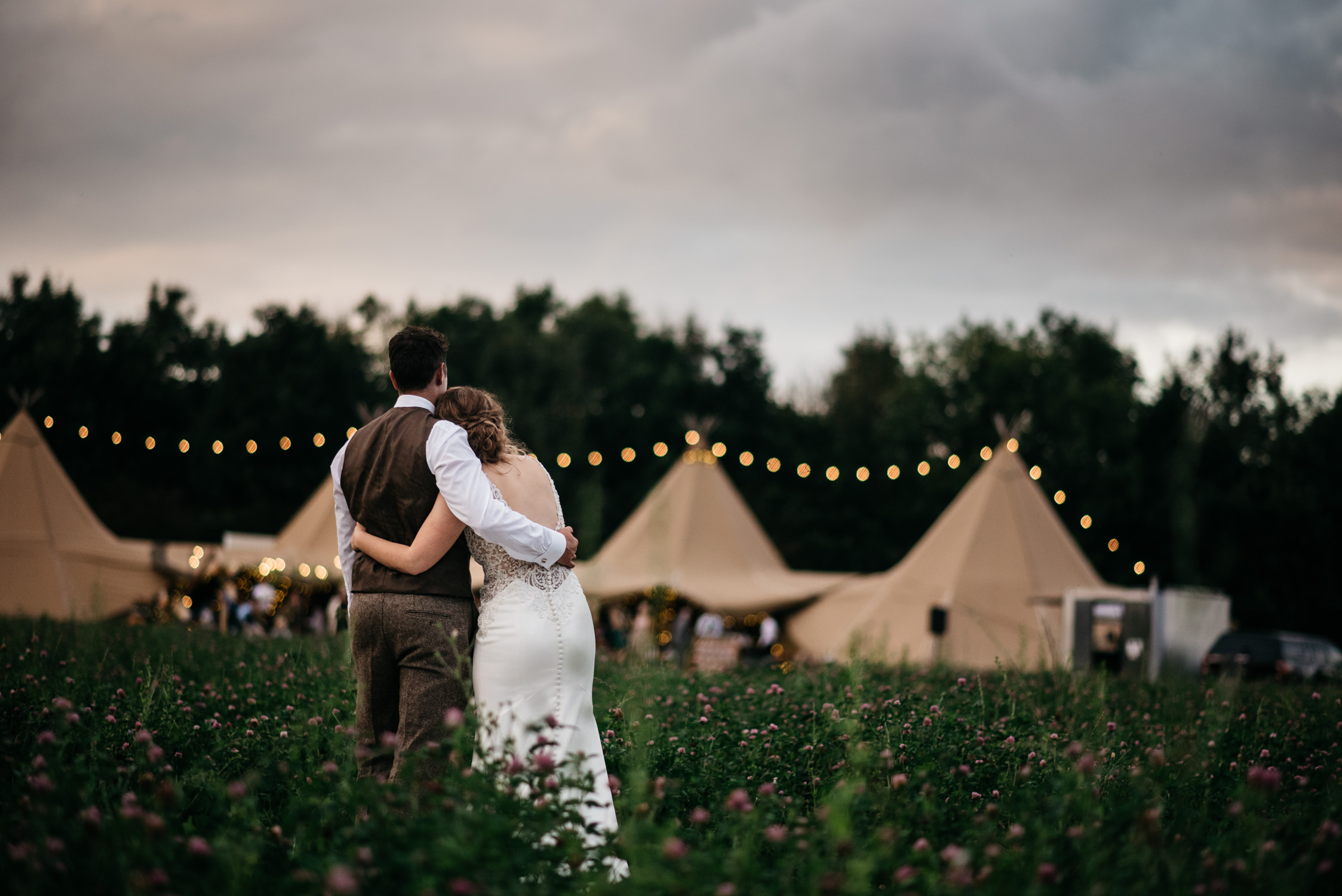 couple embrace looking back across the field at their wedding tipi
